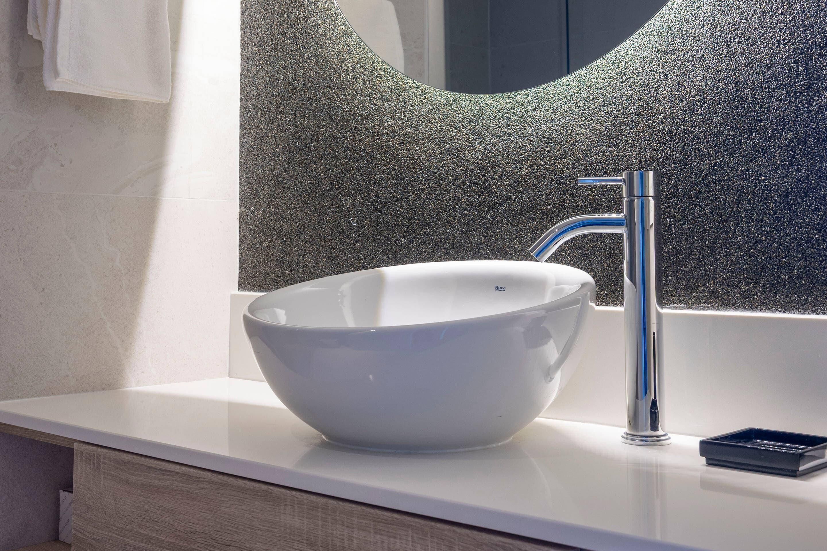 Un baño moderno con un lavamanos blanco, grifo de cromo y un espejo grande con un revestimiento texturizado.