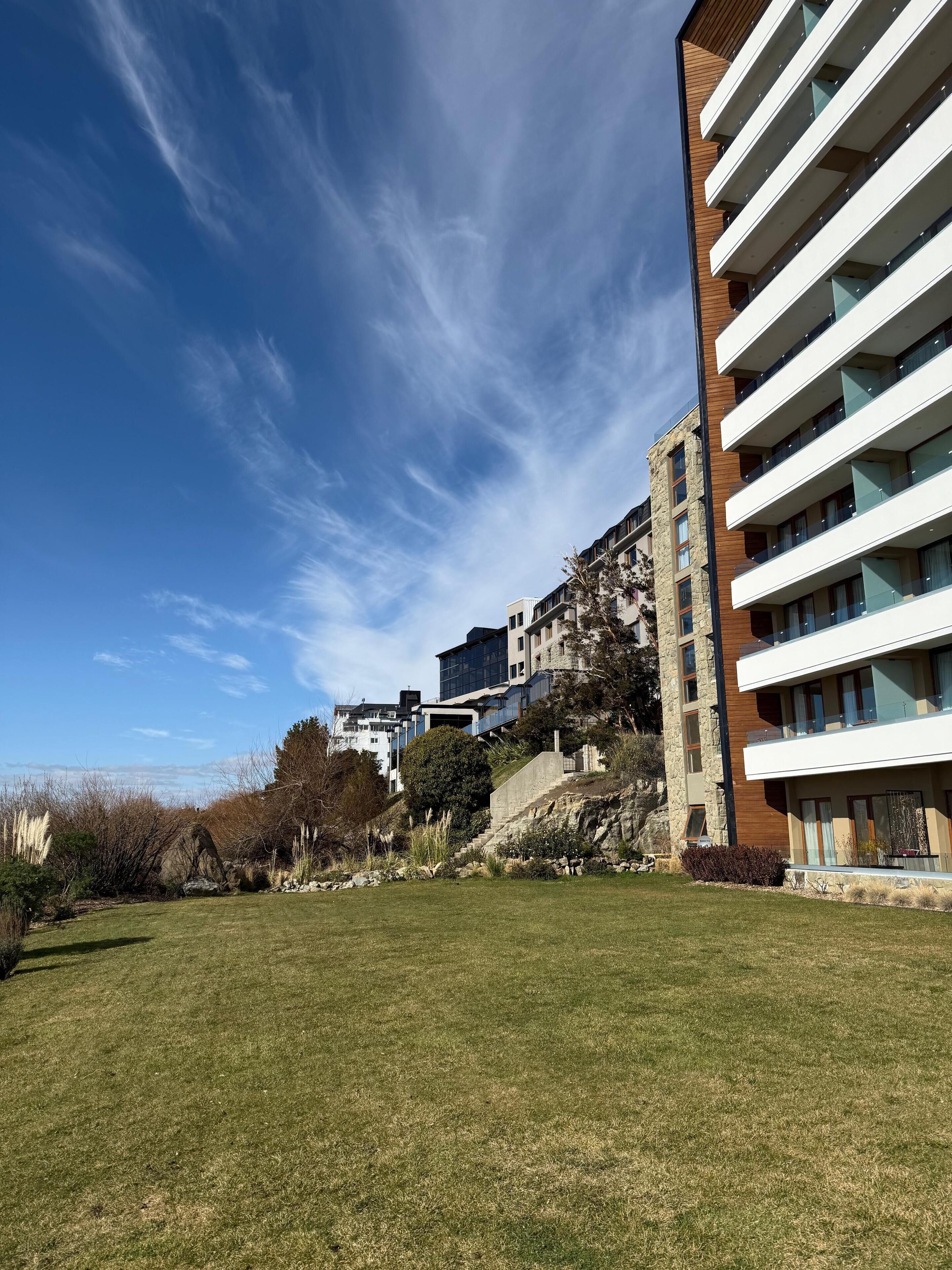 A modern apartment building with multiple balconies, a stone facade, and a grassy courtyard.