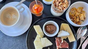A breakfast setting with coffee, fruit, cheese, and nuts on a slate plate.