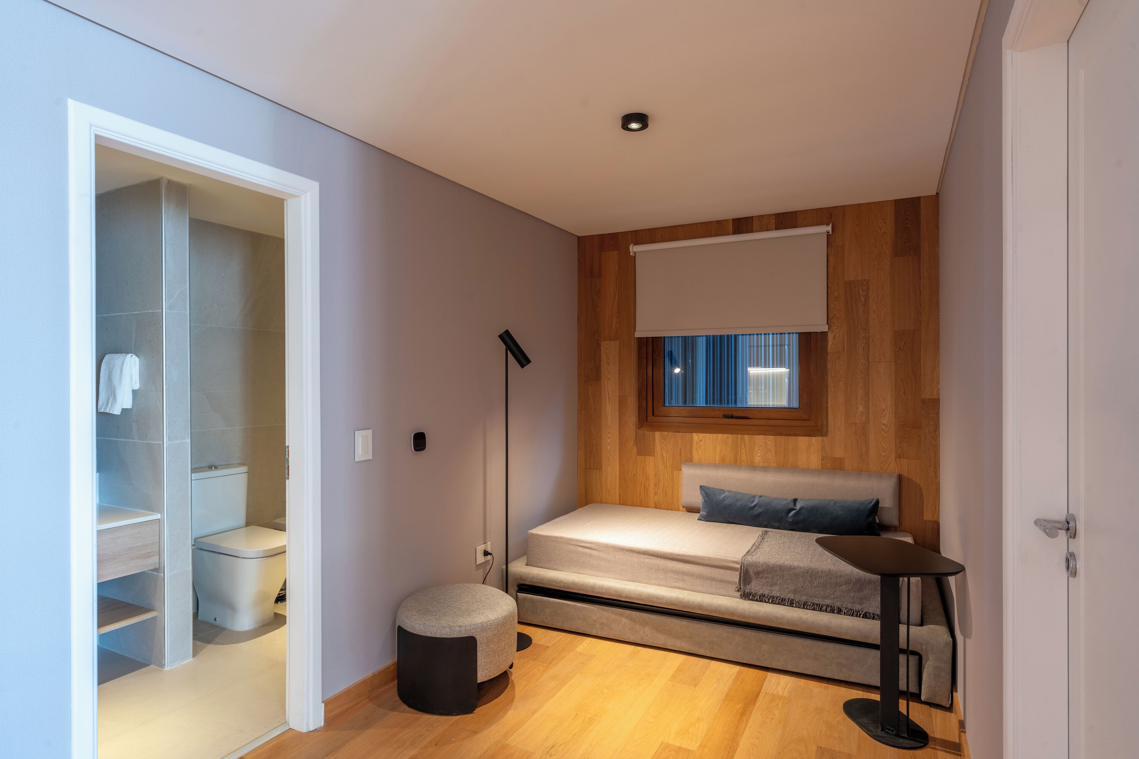 A compact bedroom with a bed, bedside table, and a window with blinds.