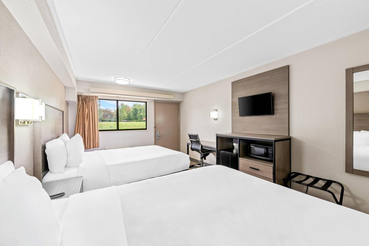 A hotel room with two beds, a desk, a chair, a flat-screen TV, and a window with curtains.
