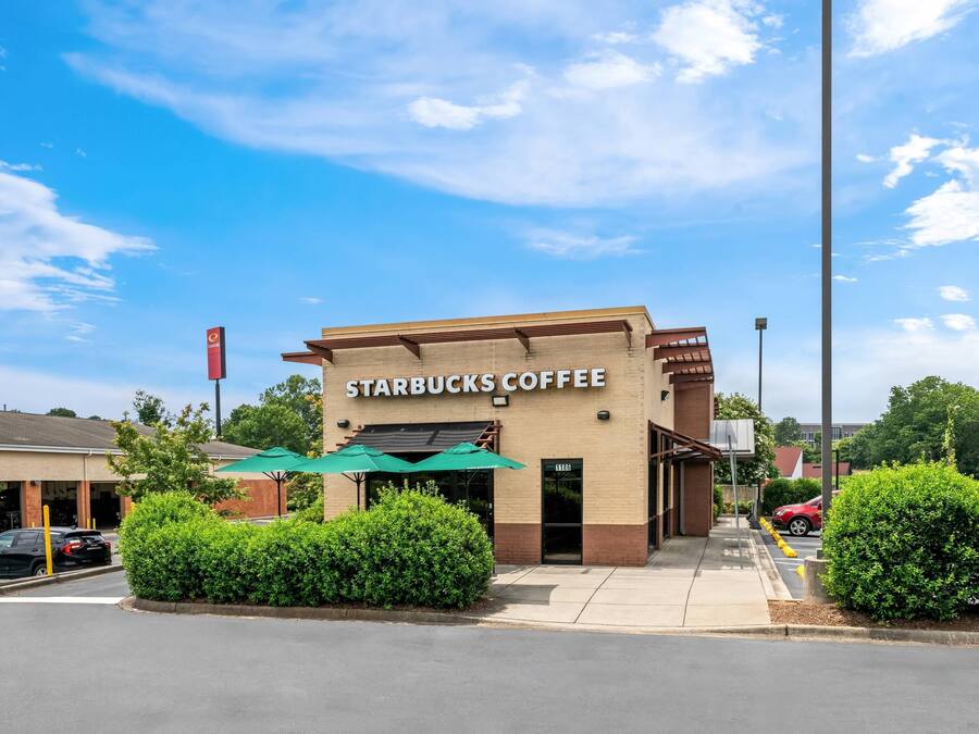 Um Starbucks Coffee com uma placa visível, um guarda-chuva verde e um estacionamento.