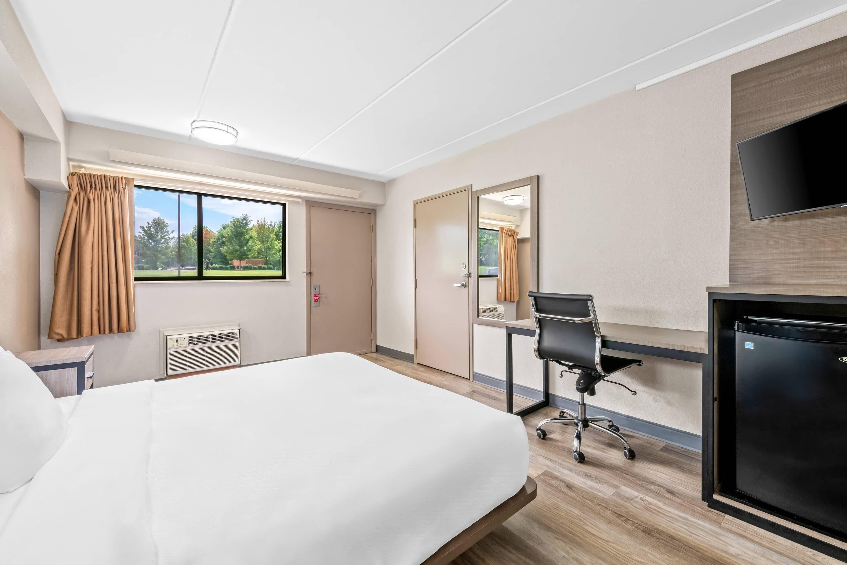 A hotel room with a bed, desk, chair, and a TV.