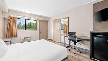 A hotel room with a bed, desk, chair, and a TV.
