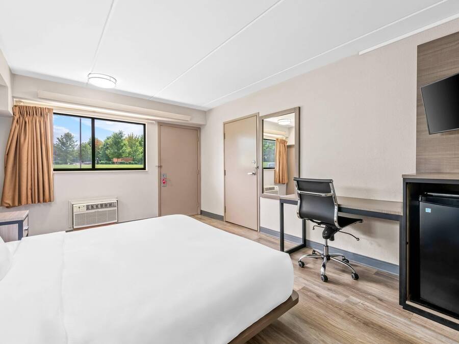 A hotel room with a bed, desk, chair, and a TV.