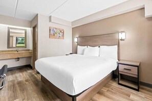 Een hotelkamer met een groot bed, een nachtkastje met een lamp, een klein bureau en een stoel.