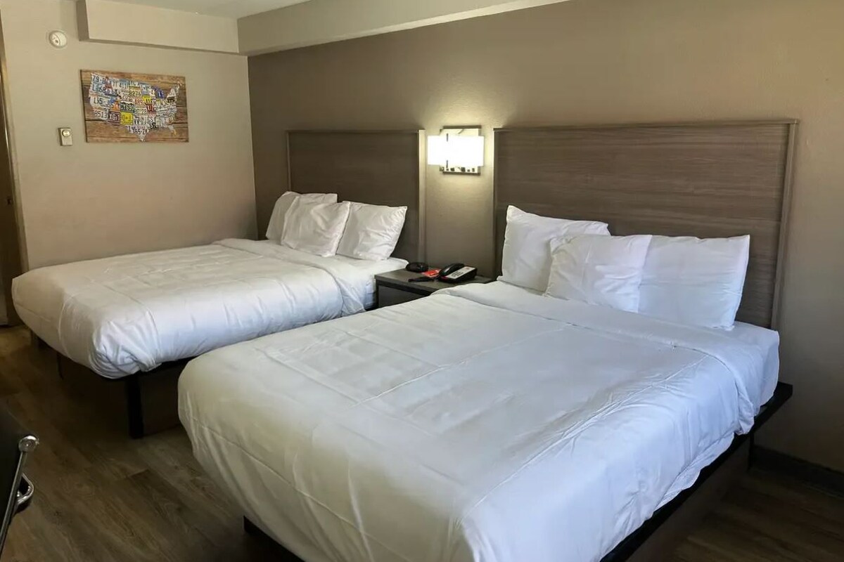A hotel room with two beds, a nightstand, a lamp, and a wall art piece.