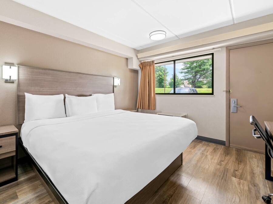 A hotel room with a large bed, a nightstand, a dresser, and a window with curtains.