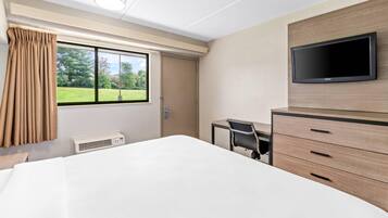 Habitación de hotel con cama, escritorio, silla, televisor y ventana con cortinas.