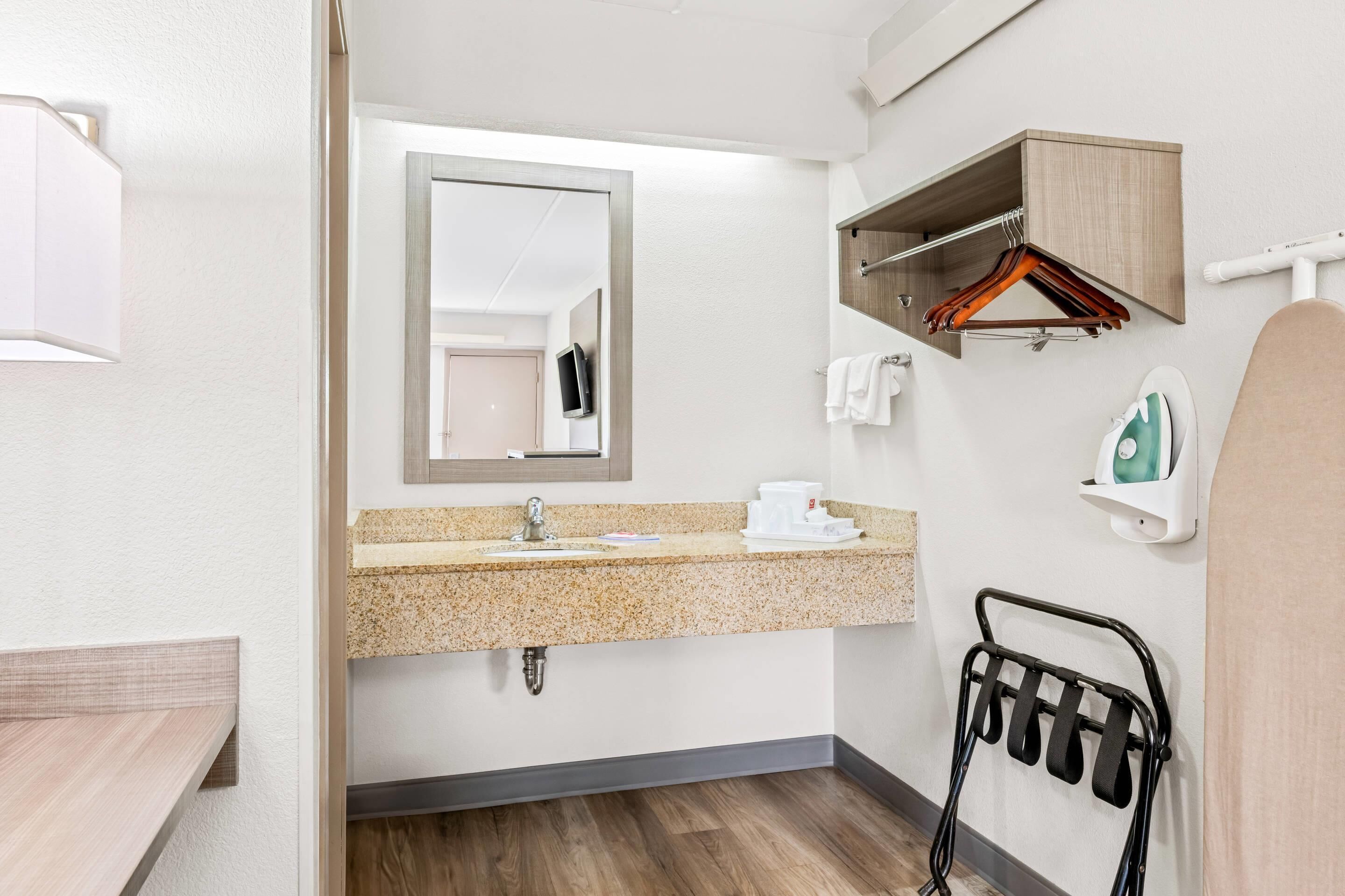 A modern bathroom with a granite countertop, a mirror, a towel rack, a hanging clothes rack, and a shower area.