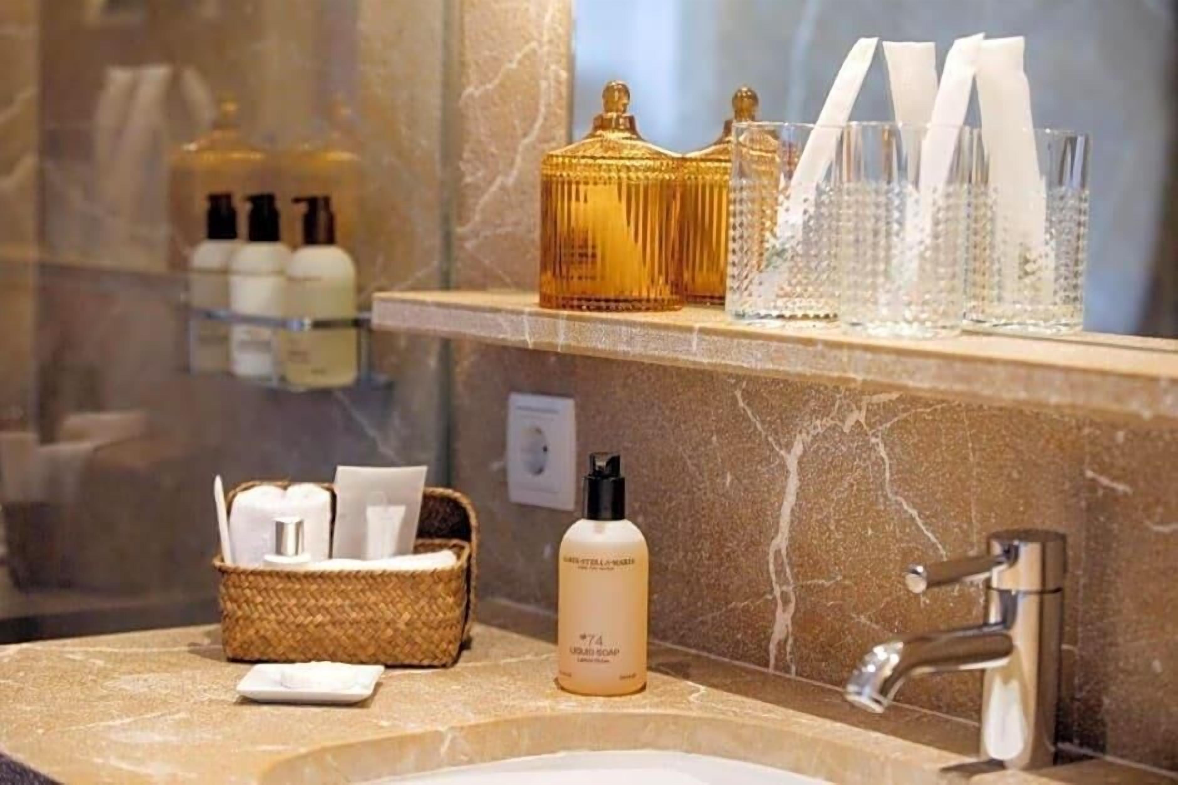 A bathroom with a marble countertop, a sink, a mirror, and toiletries on a shelf.