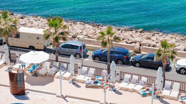 A poolside area with lounge chairs, a pool, and a view of the sea and a pier. - Portixol Hotel & Restaurant (Palma de Mallorca)