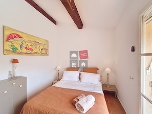 A bedroom with a bed, two bedside tables with lamps, a dresser, a painting on the wall, and a window with a view.