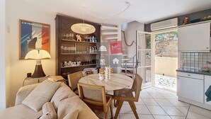 A cozy living area with a sofa, a dining table with chairs, a bookshelf, and a kitchen area with a refrigerator.