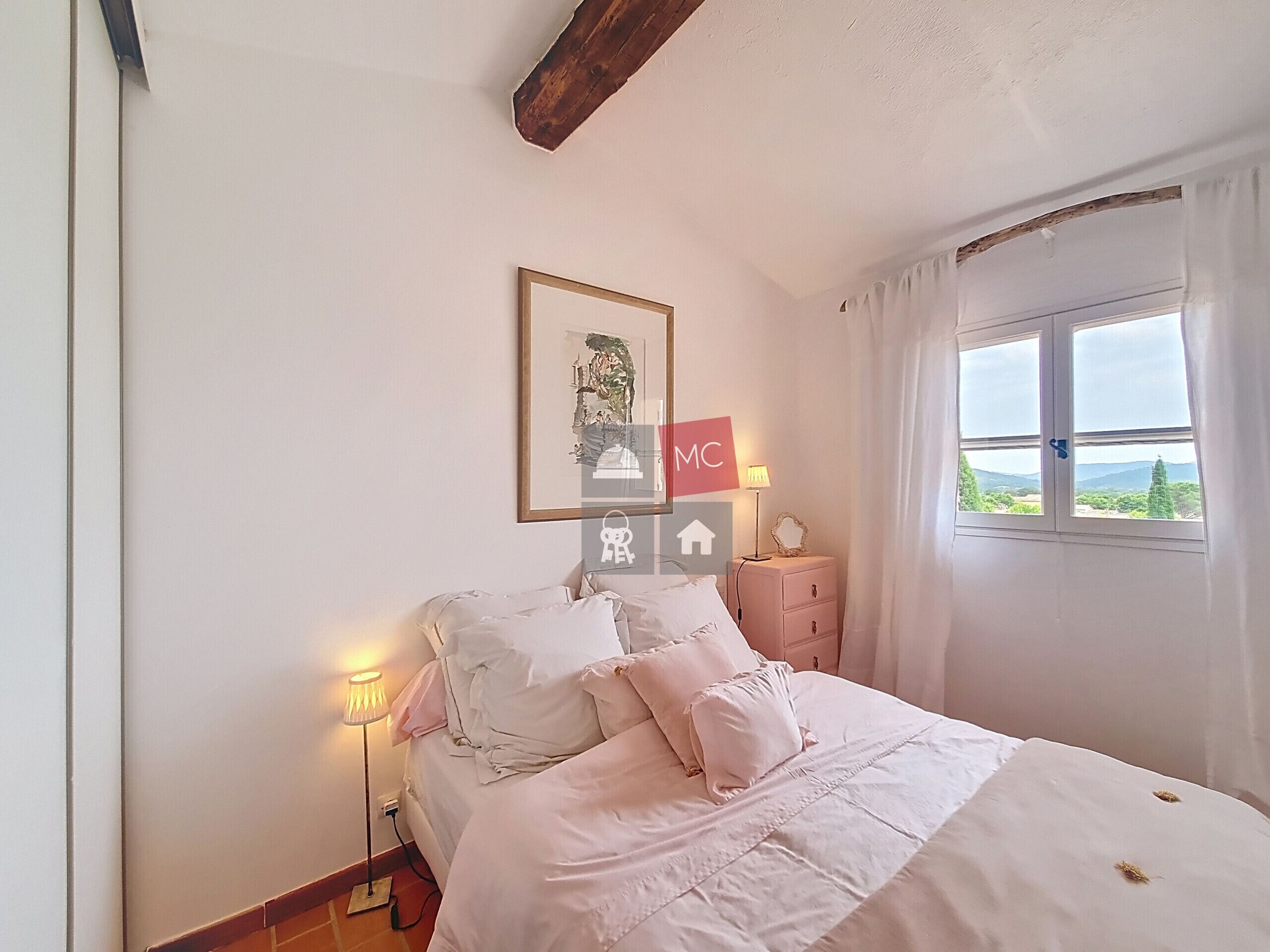 A bedroom with a bed, bedside lamps, a nightstand, a window with curtains, and a framed picture on the wall.