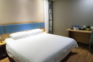 Hotellihuone, jossa on sänky, yöpöytä, työpöytä tuolilla sekä ikkuna, jossa on verhot.