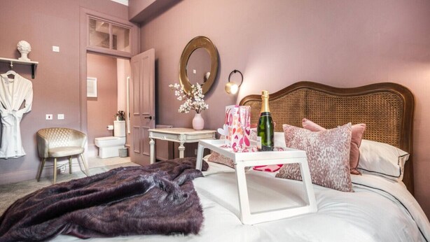 A bedroom with a bed, a bedside table with a bottle and glasses, a chair, a vanity, and a mirror. - B HOME STAY Blossom Lux Studio, Glasgow /  Airport (Paisley)