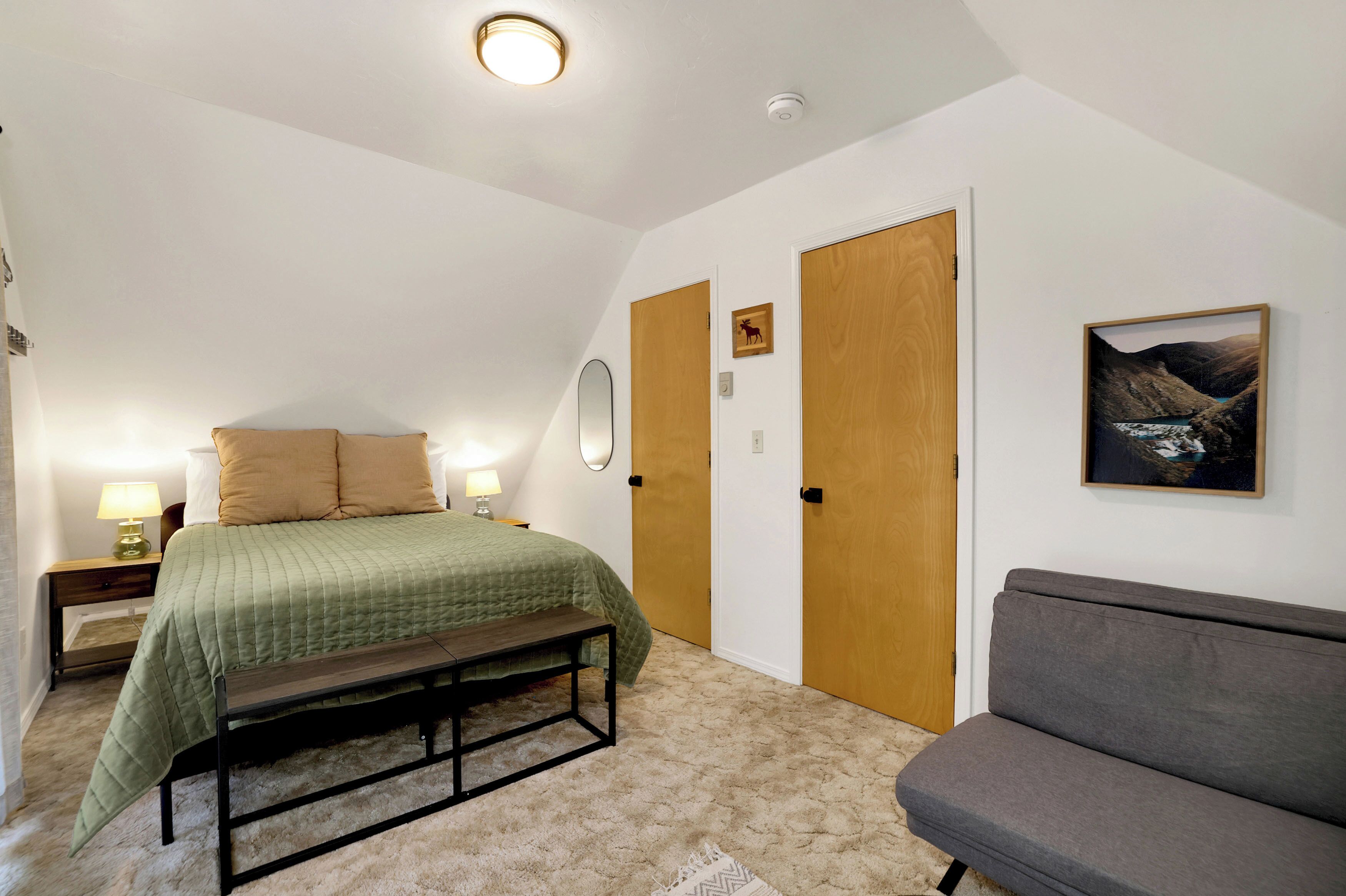 Un dormitorio con cama, lámparas de noche, un banco, un sofá y un cuadro en la pared.