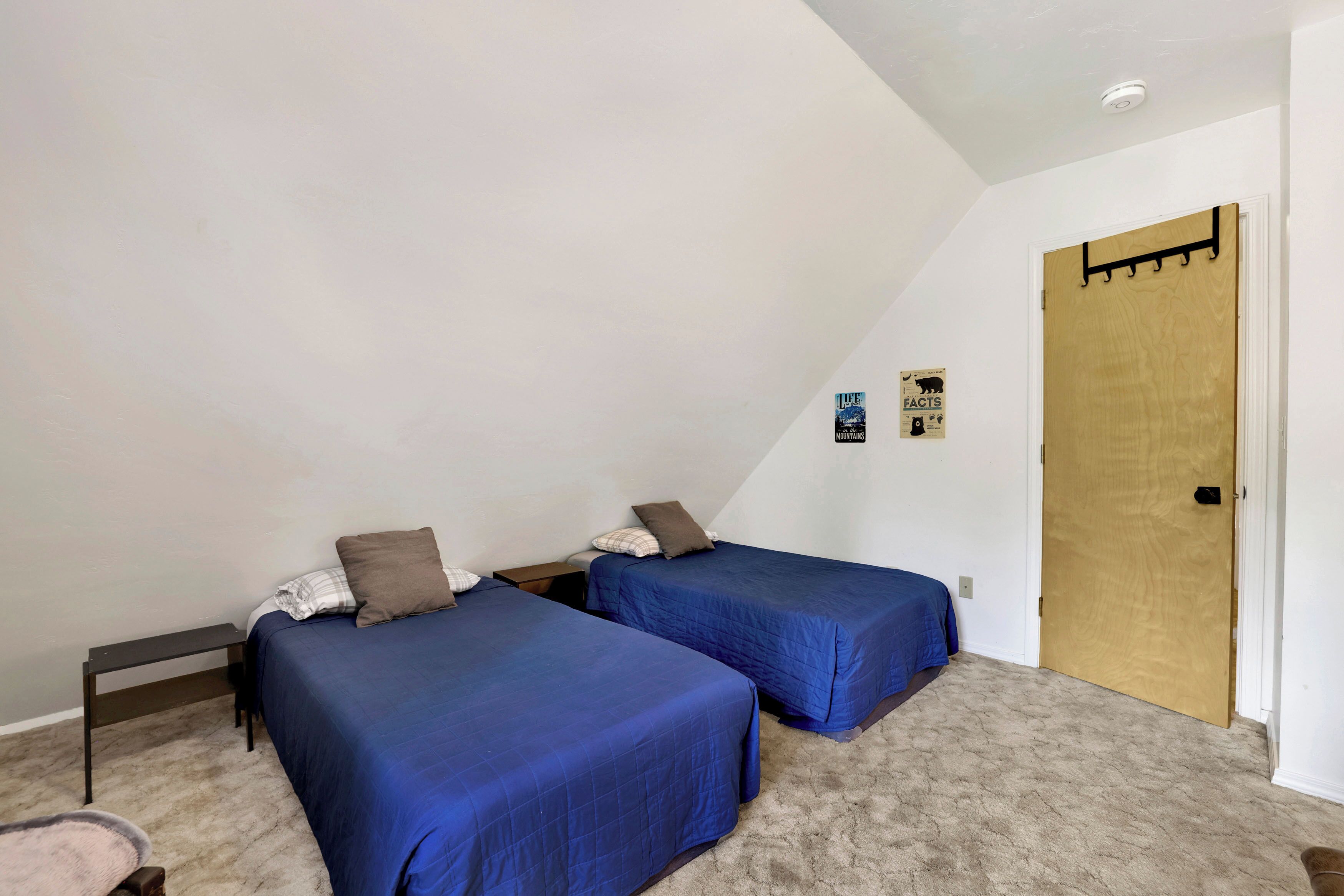 Een slaapkamer met twee bedden, een houten deur en een klein wandplankje.