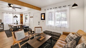 Amplia sala de estar con techo de madera, zona de comedor y ventanas grandes con cortinas de gasa.