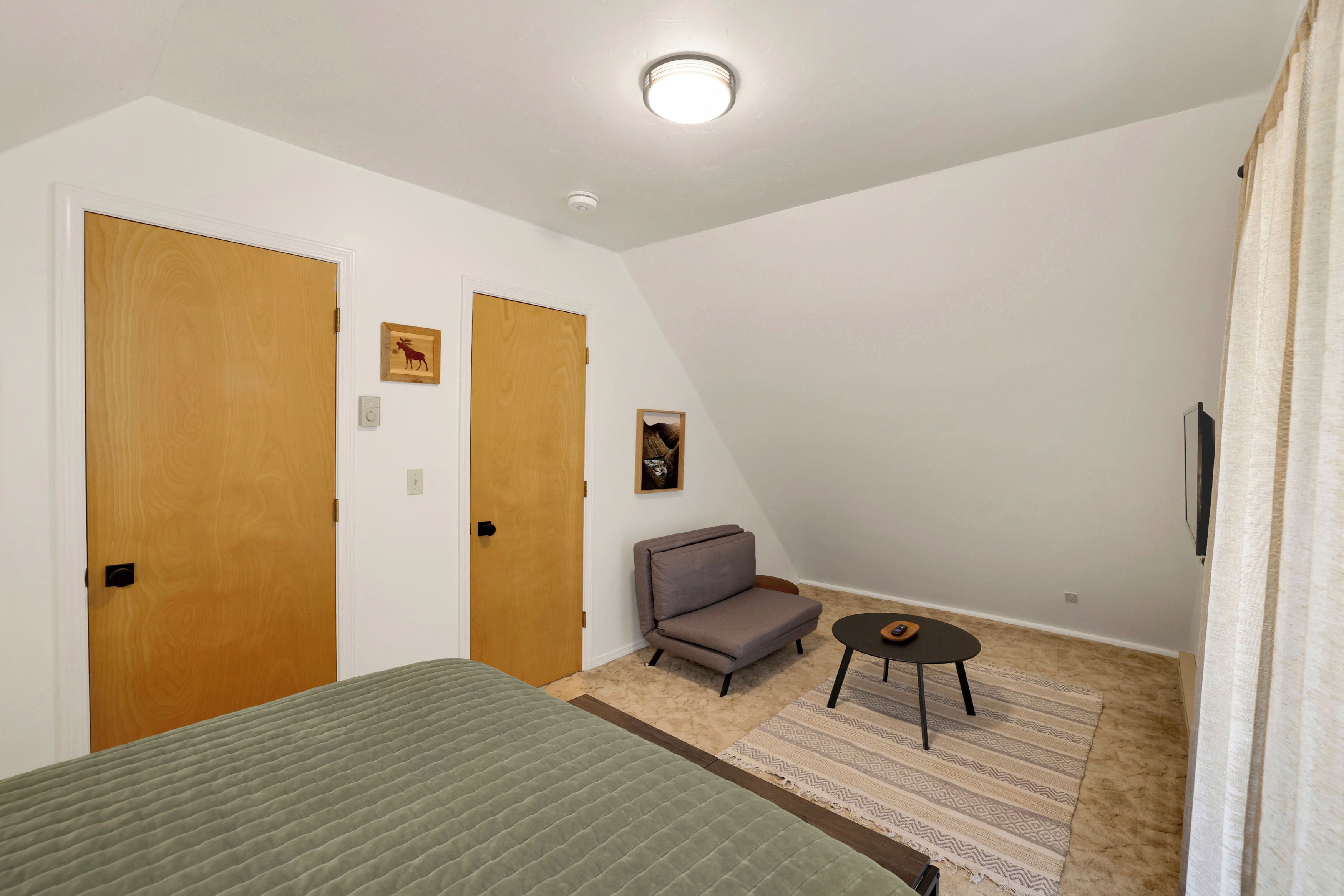 A bedroom with a bed, a sofa, a small table, and two doors.