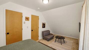 A bedroom with a bed, a sofa, a small table, and two doors.