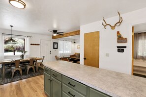 Une cuisine avec une table à manger en bois, des chaises et un grand îlot central doté d’un plan de travail en marbre.