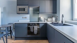 Une cuisine moderne avec des meubles de couleur sombre, un four encastré, un four à micro-ondes et un évier.