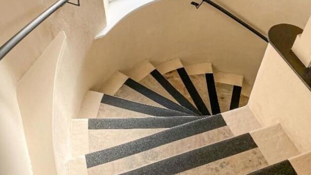 Un escalier en colimaçon aux murs de couleur beige, avec une fenêtre en haut.
