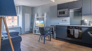 Une cuisine moderne avec des armoires grises, un four à micro-ondes et un four encastré. On y trouve un petit coin repas avec une table et des chaises, ainsi qu’un tableau accroché au mur.