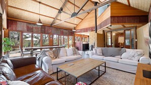A spacious living area with a high ceiling, large windows, and a cozy seating arrangement. - The Last Straw in Katoomba (Katoomba)