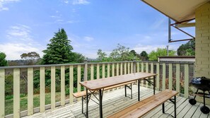 Eine Holzterrasse mit Tisch und Bänken, die auf einen Garten mit Bäumen und einem klaren Himmel blickt.