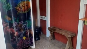 A room with a red wall, a wooden bench, a tiled floor, and a curtain with an underwater scene.
