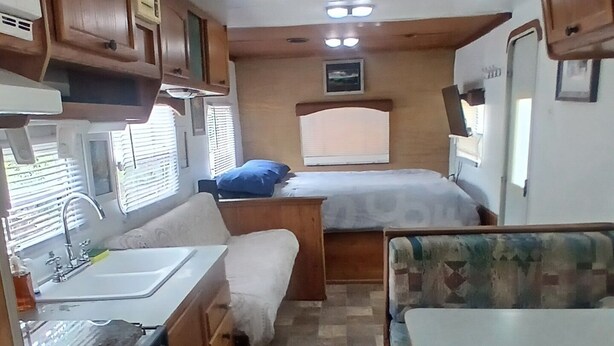 A compact RV interior with a kitchenette, a bed, and a seating area.