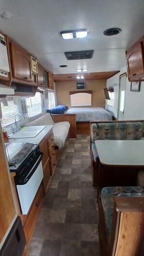 Ein kompaktes Wohnmobil-Interieur mit Küchenzeile, einem Bett und einer Sitzecke.
