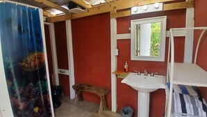A bathroom with a red wall, white fixtures, a wooden bench, and a shower curtain with an underwater scene.
