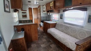 A compact RV interior with a kitchenette, a sofa, and a window with blinds.