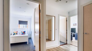 Un couloir avec un banc blanc, un miroir et une porte en bois.