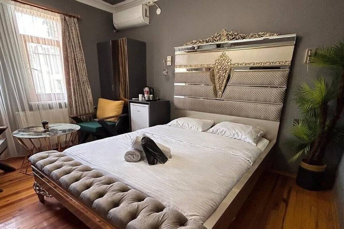 A hotel room with a large bed, a desk, a chair, a small table, and a potted plant.