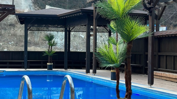 En swimmingpool med træterrasse, omgivet af plantekasser og et overdækket siddeområde.