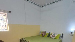 A small, single-bed room with a green bedspread, a wooden floor, a small round table, and a chair. - Hype Hostel Udaipur (Udaipur)