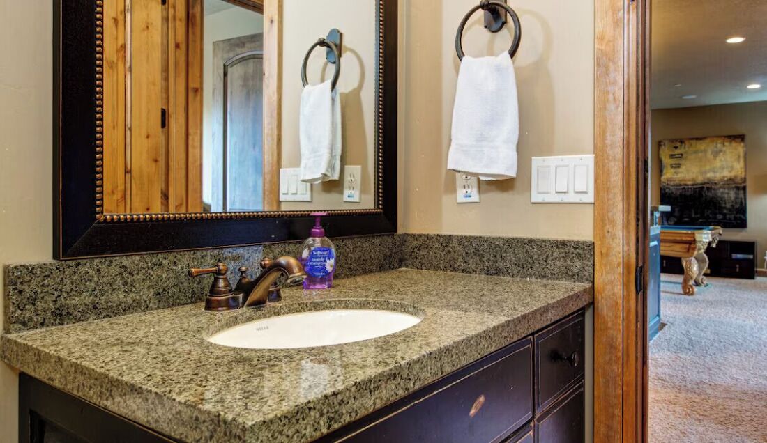 Une salle de bain avec un comptoir en granit, un lavabo, un miroir et un porte-serviettes.