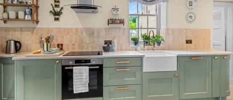 Una cocina con horno empotrado, placa de cocina y pileta. Hay armarios con pomos de madera y un ventanal con un frente decorado.