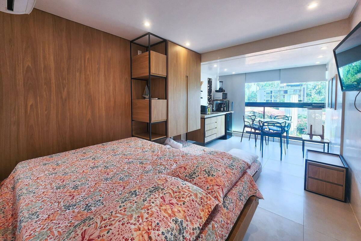 Ein Schlafzimmer mit Bett, Holzschrank, einer Küchenzeile und einem Balkon mit Tisch und Stühlen.