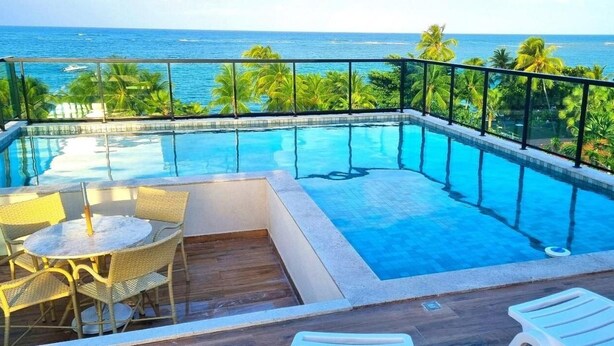 A rooftop infinity pool with a view of the ocean, surrounded by palm trees and furnished with outdoor seating. - Rooftop Tamandaré - Praia dos Carneiros (Tamandaré)