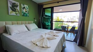 A hotel room with a bed, two pillows, a towel, a green wall, and a balcony with chairs. - Rooftop Tamandaré - Praia dos Carneiros (Tamandaré)