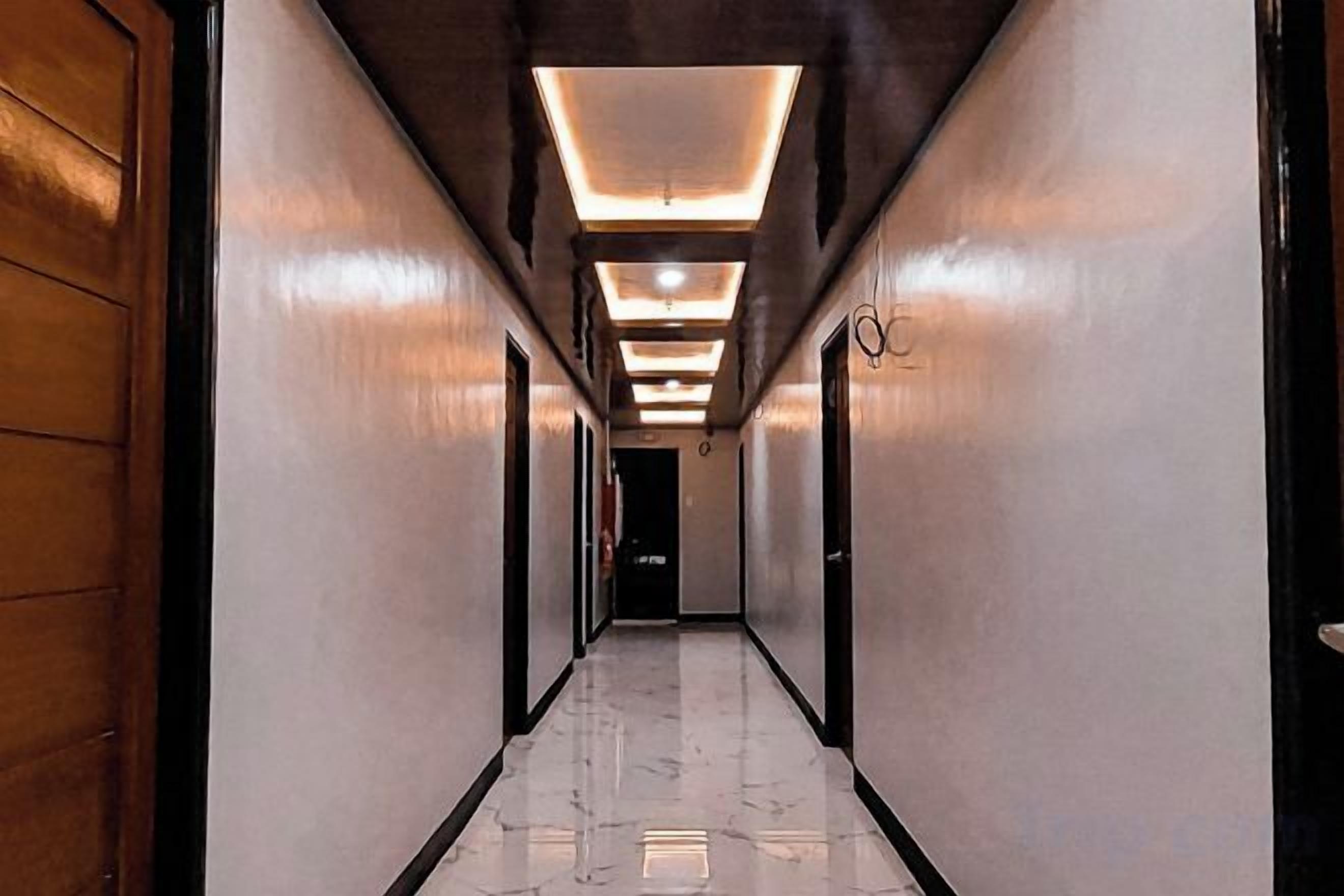 A long, narrow hallway with a polished marble floor, wooden doors on one side, and recessed lighting on the ceiling.