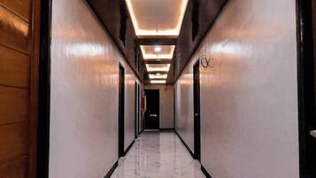 A long, narrow hallway with a polished marble floor, wooden doors on one side, and recessed lighting on the ceiling.