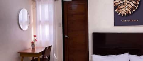 Habitación de hotel con cama, puerta de madera, mesa de comedor con sillas, espejo y aire acondicionado instalado en la pared.