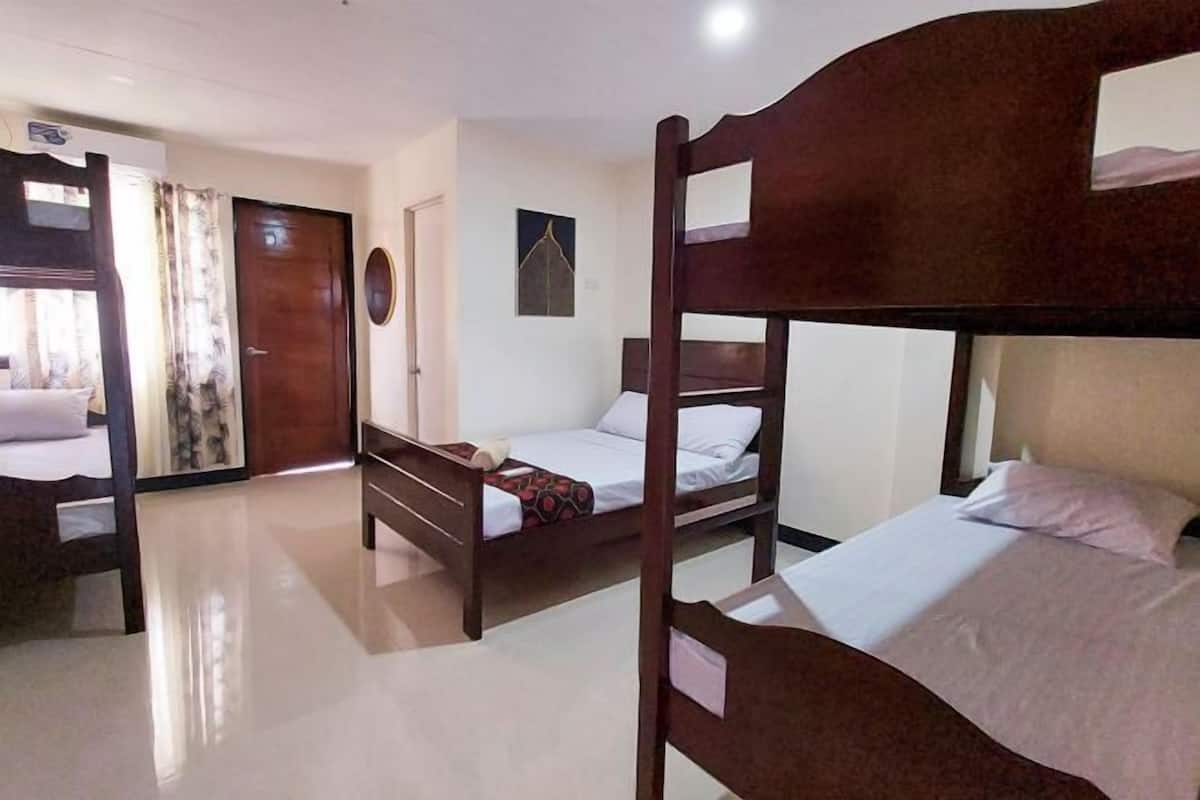 Una habitación de hotel con literas, una puerta, un reloj fijado a la pared y una ventana con cortinas.